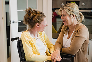 Home Care Personal Care A carer laughs with a young woman in a wheelchair