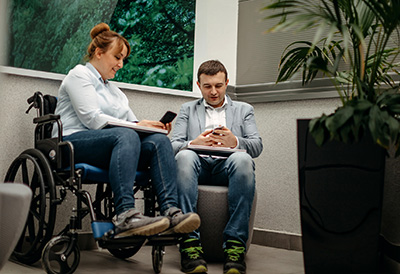 Medical Visits A wheel chair user and assistant check their phones while waiting for the doctor.